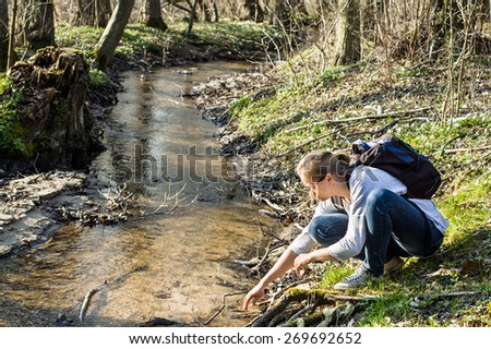 Young woman hiker with backpack by the river in the spring forest, outdoor activities and leisure