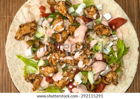 Tortilla with grilled meat and vegetables on bamboo mat background