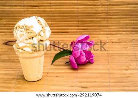 Scoop of ice cream in a waffle cone and peony flower as symbol of summer and holiday on wood background