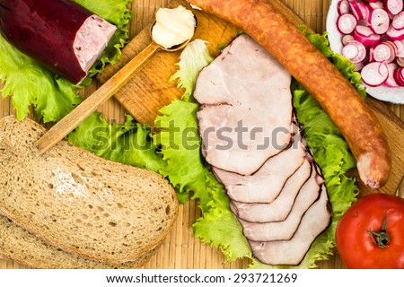 Sausages and slices of sausage with vegetables and bread for breakfast or dinner on cutting board and bamboo mat.