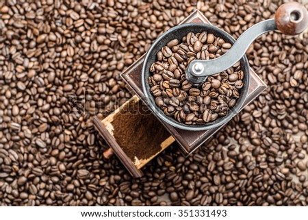 Manual coffee grinder on background of blurred coffee beans, top view.
