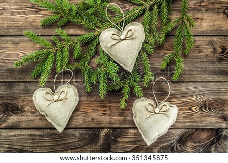 Decorative pillows shaped heart hanging on christmas tree on wood background.