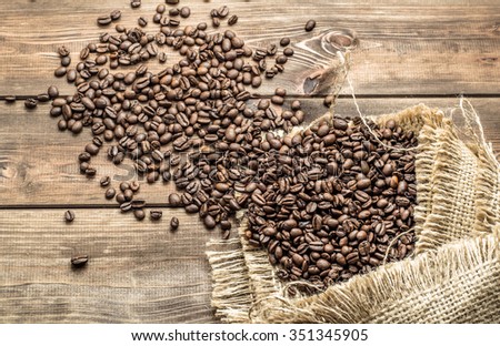 Black coffee beans in burlap sack on wooden table, selective focus.