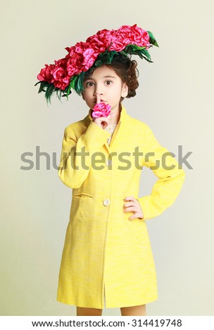 Beautiful little girl in yellow coat and funny hat with roses. Studio shot