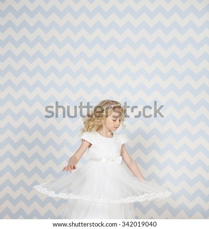 Little fairy angel in white fashion dress smiling in motion. Blue background.  Copy space