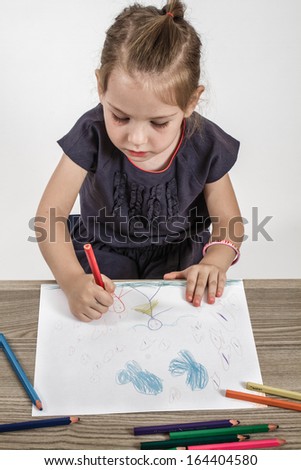 Blond cute little girl painting on a school desk in front of white background
