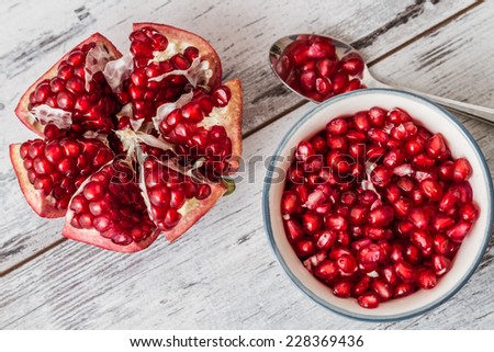 Pomegranate seeds in a plate and half pomegranate on a white wooden background