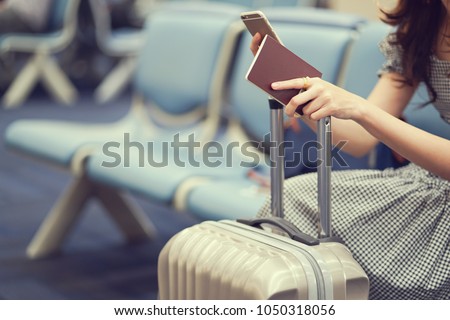 close up woman hand holding passport and playing smartphone on her suitcase at airport while waiting for boarding time ,traveler concept