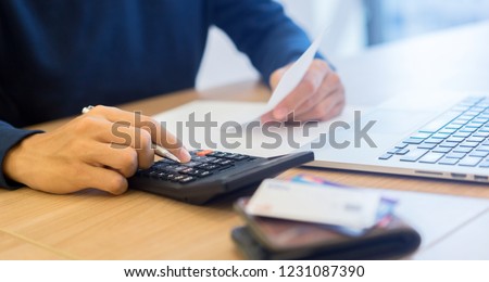 close up man hand writing on notebook and calculating on calculator about debt bills monthly at the table in home office and managing expense payroll,money risk financial concept