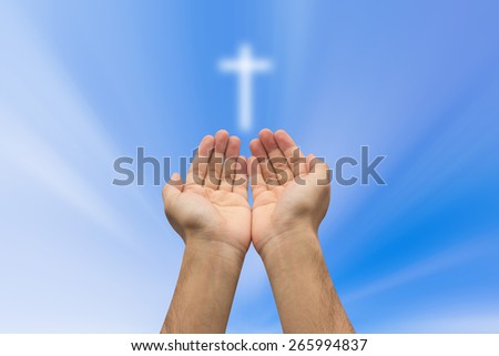 Two hands  pray with cross blurred sky background , soft focused.