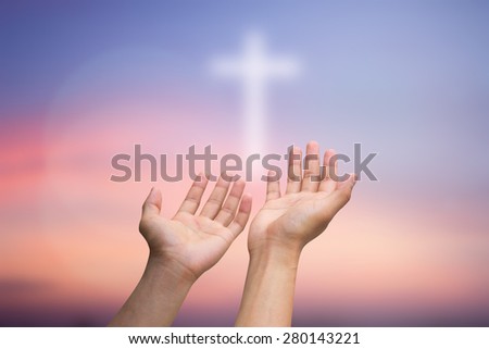 human\'s hands praying with cross blurred twilight sky background , soft focused.