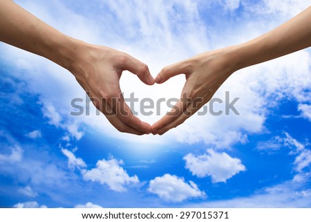 close up male and female hands making heart on blurred blue sky backgrounds . passion in love concept ,soft focused