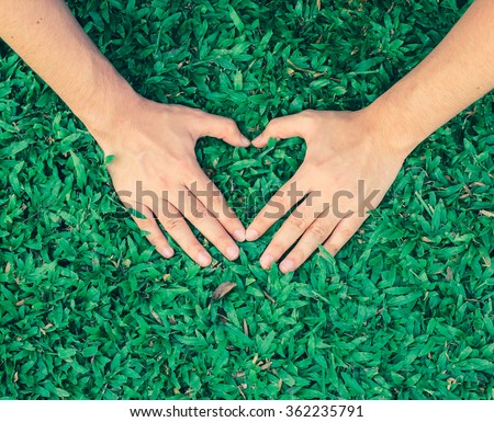 close up and selective focus on man hands make heart shape on green grass background in vintage effect:soft focus love heart on garden park outdoor concept:love environment/ecology/world:cropped image