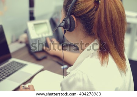 close up call centre woman working in office room:focus on headphone of asian girl response/answer customer\'s question or partner concept:people with technology and innovation:vintage filter effect.