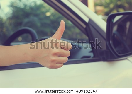 close up woman hand showing thumb up through car\'s window:safety and assurance of driving concept:image in vintage filter effect:save life insurance.stop accident