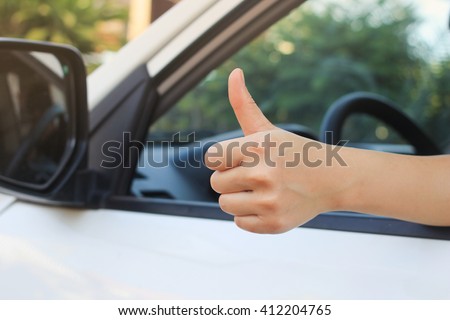 close up woman hand showing thumb up through car's window:safety and assurance of driving concept:image in vintage filter effect:save life insurance.stop accident:good drive concept idea.