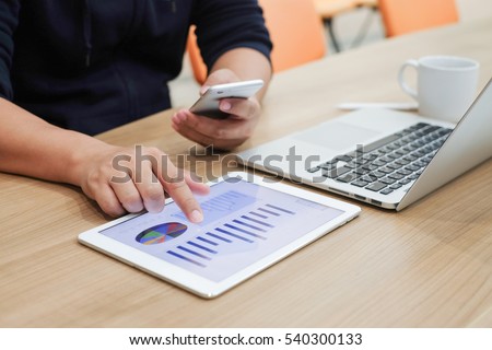 Close up employee hand point review on tablet use smart phone with laptop on desk.busy officer doing many job concept:business technology.strategy planning:work hard:analyst solution:multitask:company