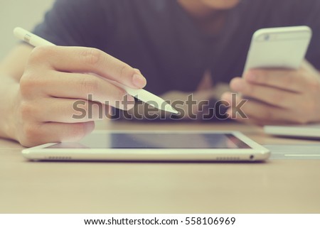 Close up asian man hand holding smartphone and using smart-pen technology for writing on tablet portable:multitask people working with multimedia device for test or play before review in blog