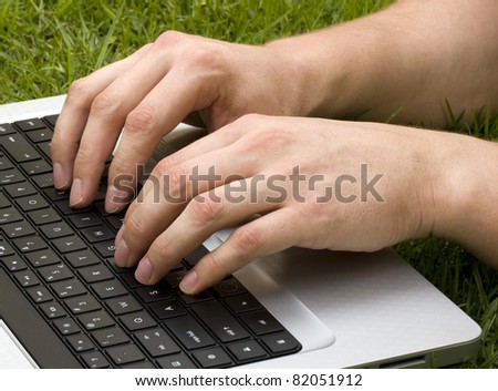 White male fingers typing on a notebook on a lawn