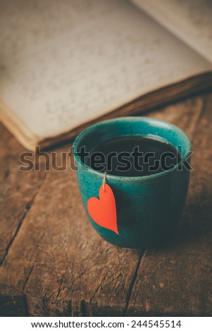 Tea cup with a red heart and an old journal on an old wooden table