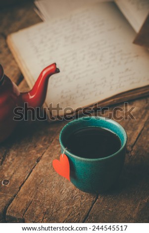 Tea cup with a red heart , teapot and an old journal on an old wooden desk