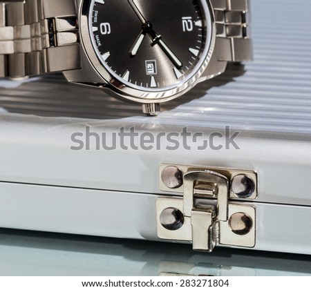 Business still-life, a fragment of a wristwatch, metal case on bright background.
