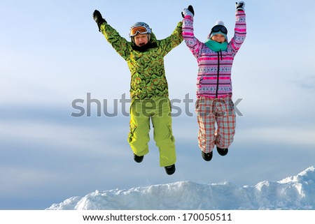snowboarders friends in bright vivid clothes jumping in snow with mountains on background