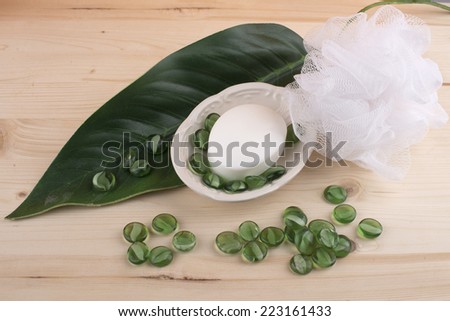 Soap-dish with soap,wisp of bast,green leafand green glass stones on the wooden table