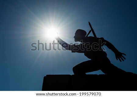 statue of a soldier grabbing backlit sun with hand