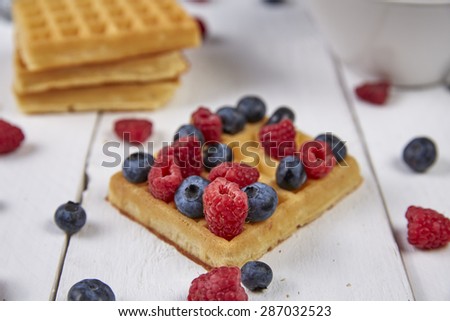 Different berries on a waffle and in a bowl on a white wooden table