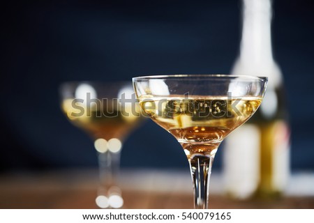 Wine glass with yellow sparkling wine in front of blue background