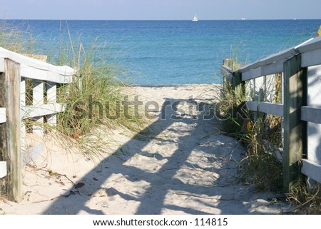 Entrance to the beach with sailboat on the ocean