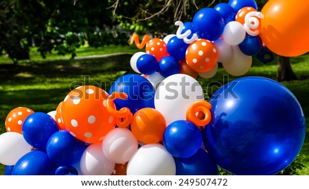 Multicolored balloons float in a park on a sunlit day.