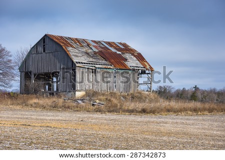An old barn with weathered gray boards and a rusty roof sits in a farm field.