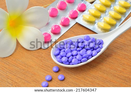 Close up many purple medicine tablet on the spoon with tablet in package ,white flower and dried tree branch on wood background