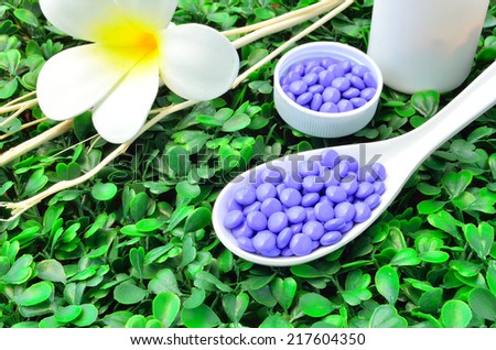 Close up many purple medicine tablet on the spoon with white flower and dried tree branch on green grass background