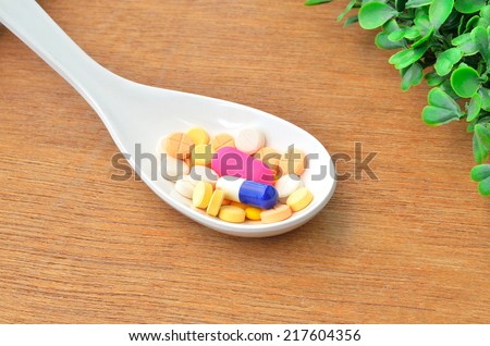 Close up many colorful medicine tablet on the spoon with green grass on wood background