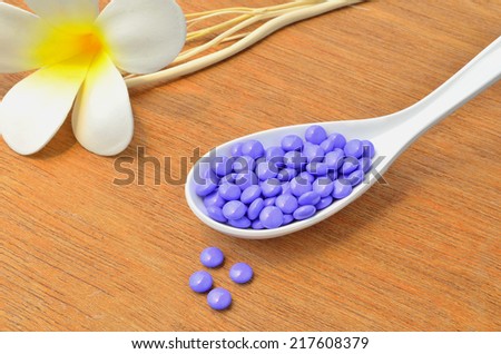 Close up many purple medicine tablet on the spoon with white flower and dried tree branch on wood background