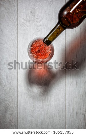 Red wine pouring into glass from bottle on white wooden table. Top view