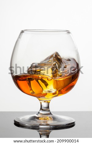 Splash of whiskey with ice in glass isolated on white background. Raw image, no postproduction