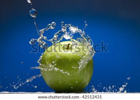 Green apple with water splash on blue background