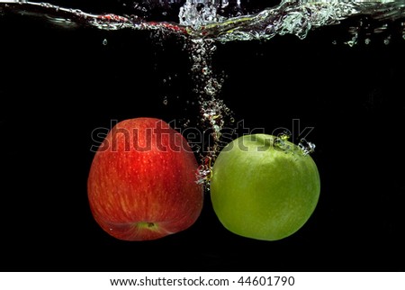 ref and green apple dropped into water with splash isolated on black