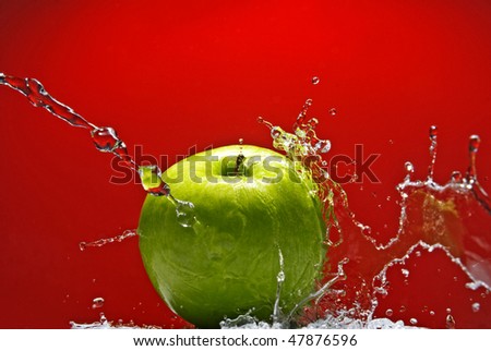 Green apple with water splash on red background