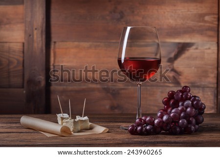 Red wine in glass with grape and cheese on wooden background