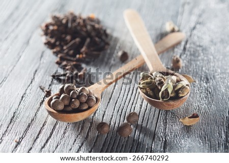 Nutmeg, clove and allspice in old spoon on wooden background. Natural raw image