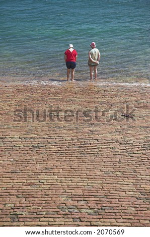 Two women test the water temperature at the seaside.