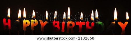 Panoramic Happy Birthday candles alight against a dark background
