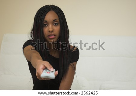Young woman with TV remote control. Focus is on her face, the remote is blurred.