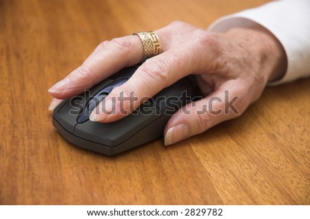Older woman\'s hand using a wireless computer mouse. Focus is on the front of the mouse / end of the fingers.