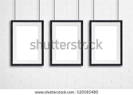Three black wooden frames, hanging on cords, against bricks wall, mock up